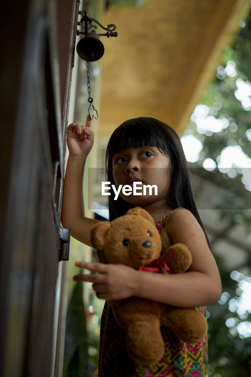 Low angle view of girl holding teddy bear standing at entrance