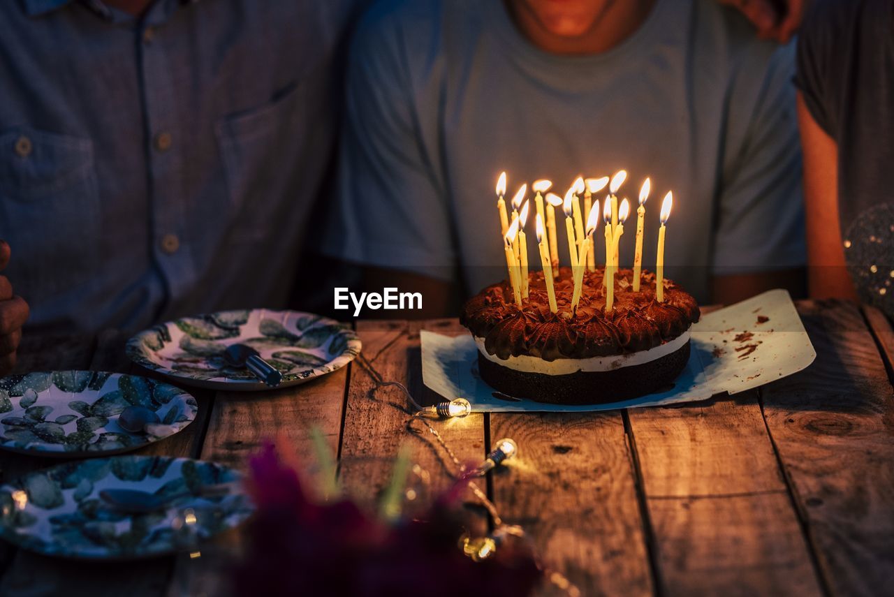 Midsection of man sitting by birthday cake