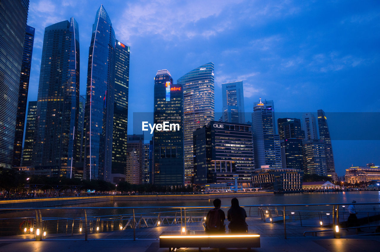 Rear view of two people overlooking tall buildings