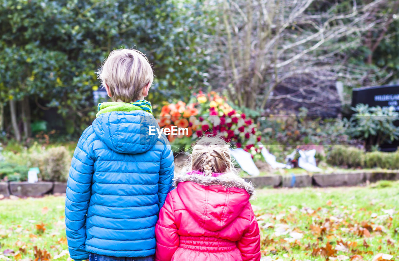 Siblings standing against flowers in graveyard