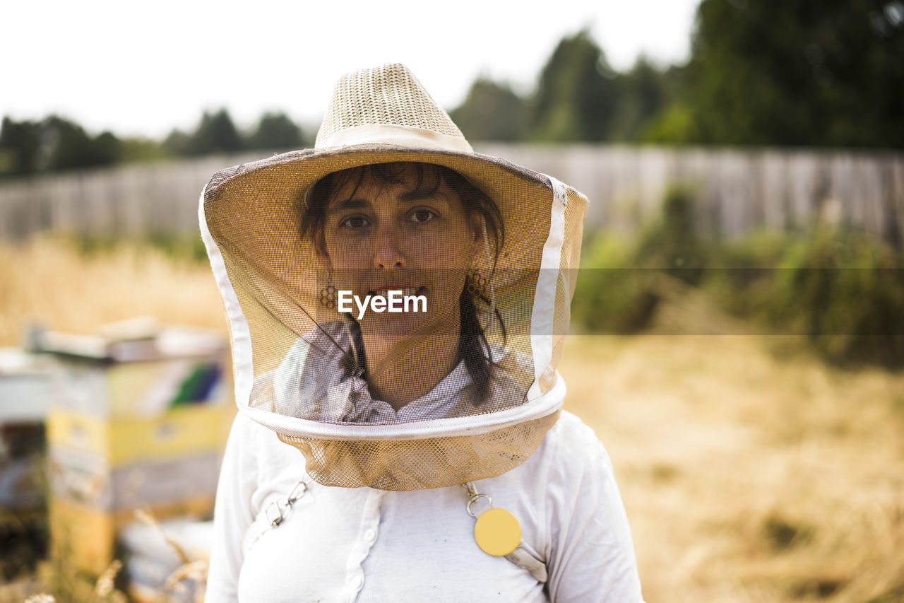 Portrait of female beekeeper wearing protective mask and hat on field