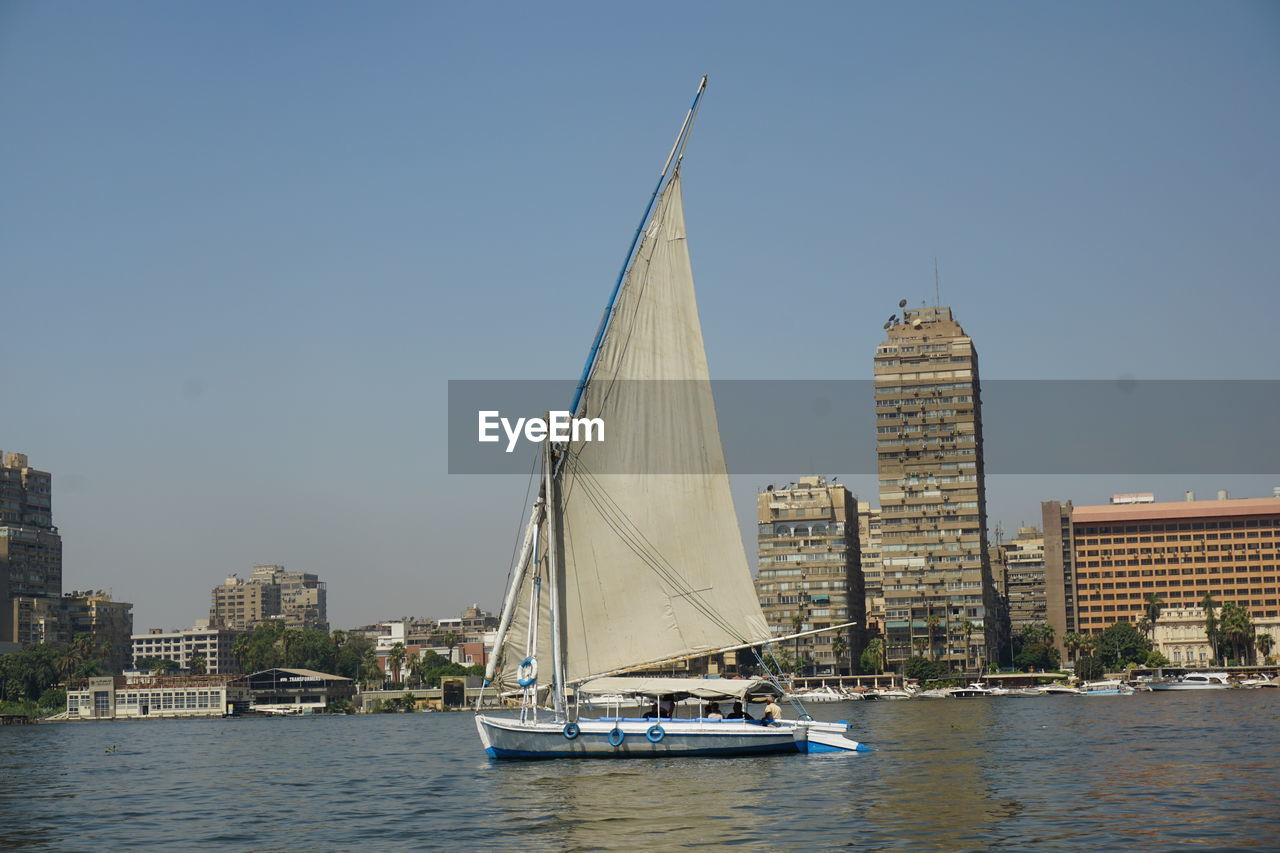 water, nautical vessel, architecture, transportation, sailboat, sailing, city, built structure, mode of transportation, building exterior, sky, boat, sailing ship, travel, building, vehicle, travel destinations, ship, sea, nature, clear sky, office building exterior, watercraft, yacht, urban skyline, cityscape, skyscraper, mast, landscape, outdoors, no people, day, luxury, waterfront, craft, tourism, blue, skyline, harbor, copy space, bay