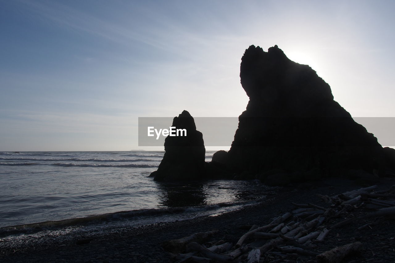 Silhouette rock formation at beach against sky during sunset