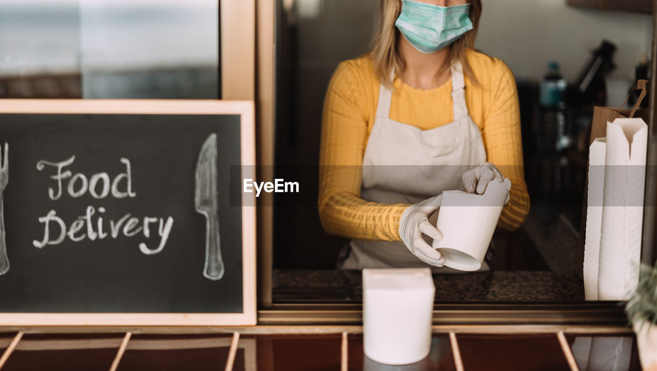 Midsection of woman wearing mask delivering food through window