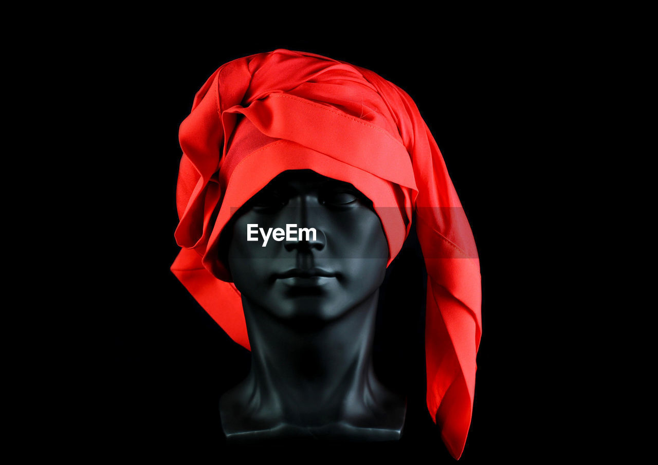 Black plastic mannequin head with large red silk scarf, black background.