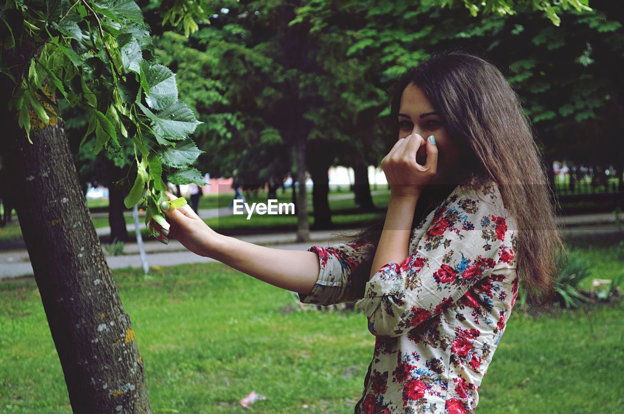 Portrait of woman standing by tree in park