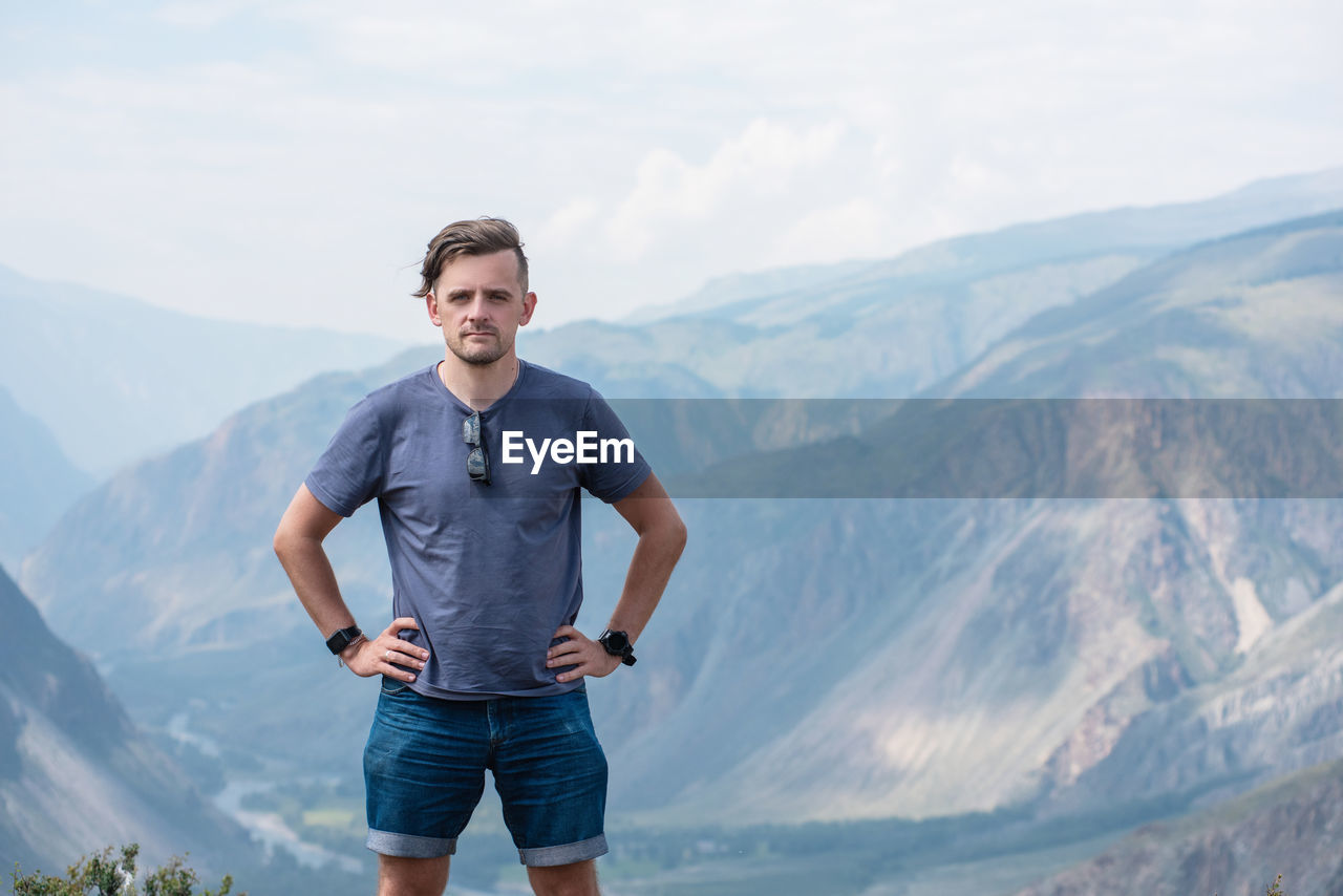 FULL LENGTH PORTRAIT OF YOUNG MAN STANDING ON MOUNTAIN
