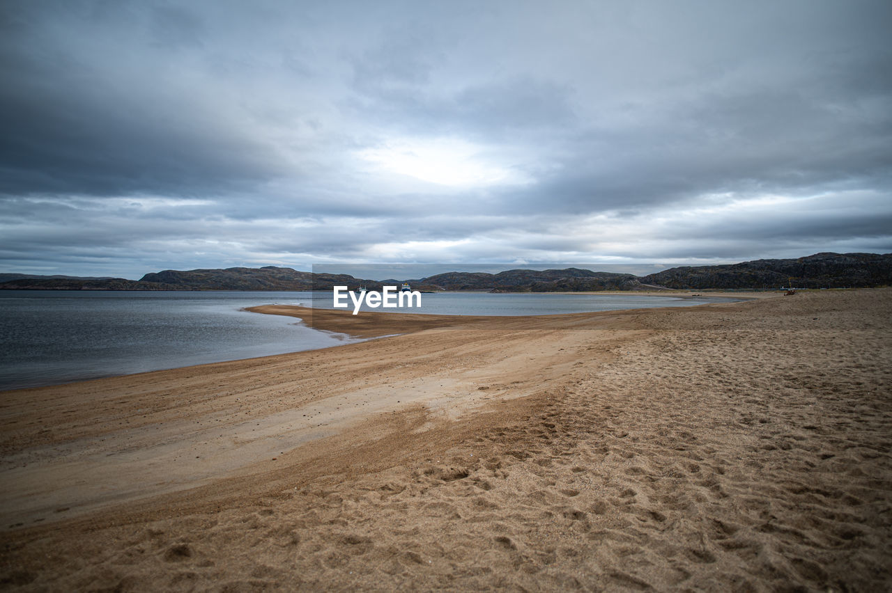 land, sky, beach, sea, water, cloud, sand, scenics - nature, environment, horizon, beauty in nature, ocean, landscape, coast, nature, body of water, shore, wave, dramatic sky, tranquility, travel destinations, coastline, travel, sunlight, mountain, no people, tranquil scene, storm, wind wave, outdoors, water's edge, overcast, seascape, tourism, non-urban scene, holiday, cloudscape, trip, vacation, storm cloud, awe, dusk, day