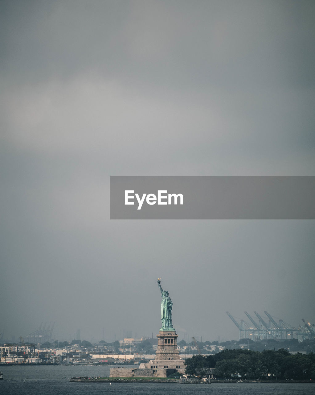 Statue of liberty by river against cloudy sky