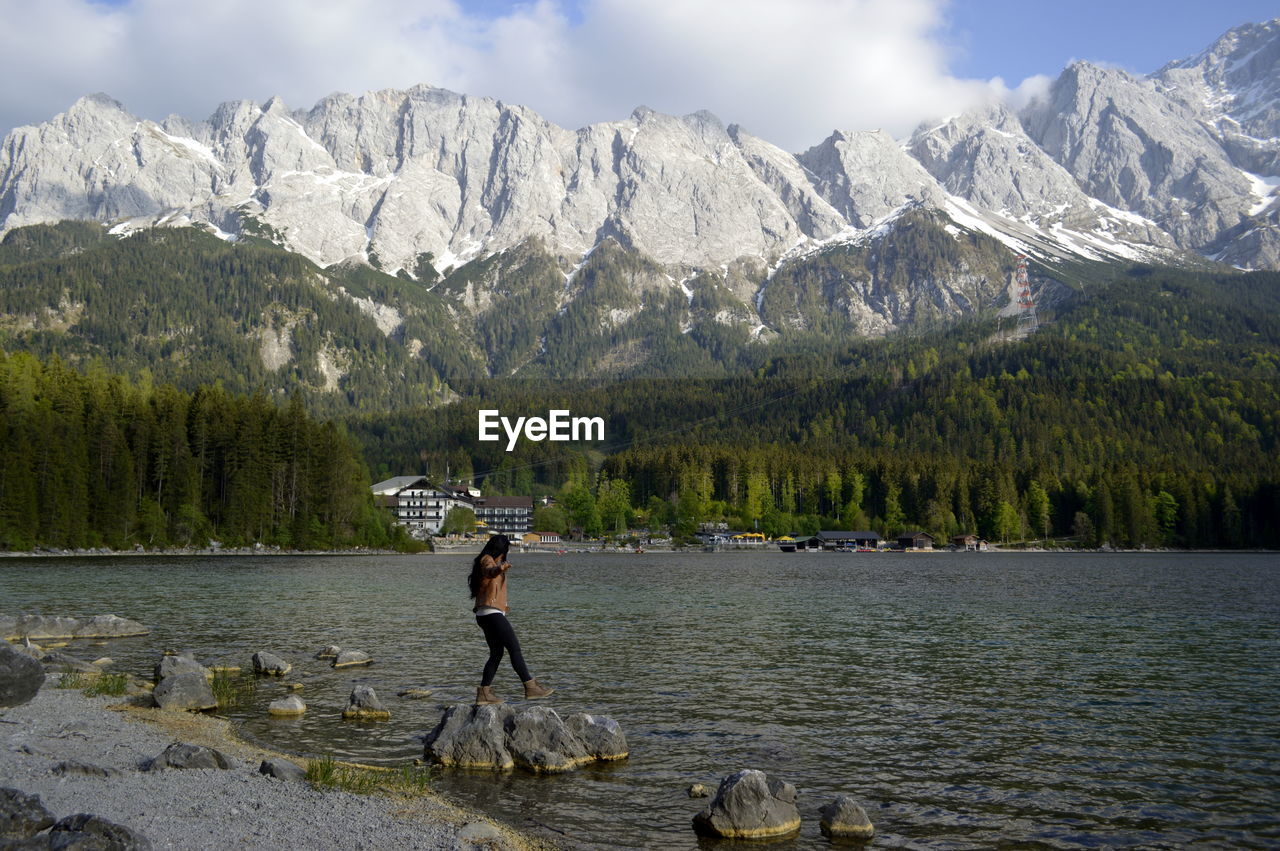 Side view of young woman walking on rocks in lake against mountains