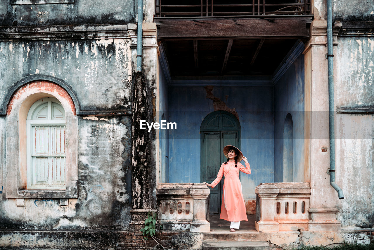 FULL LENGTH OF WOMAN STANDING BY BUILDING