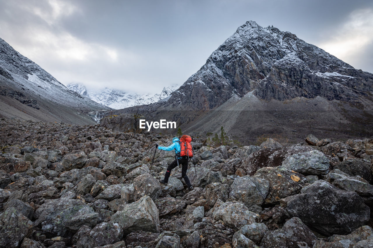 Rear view of man hiking on rock formation against sky