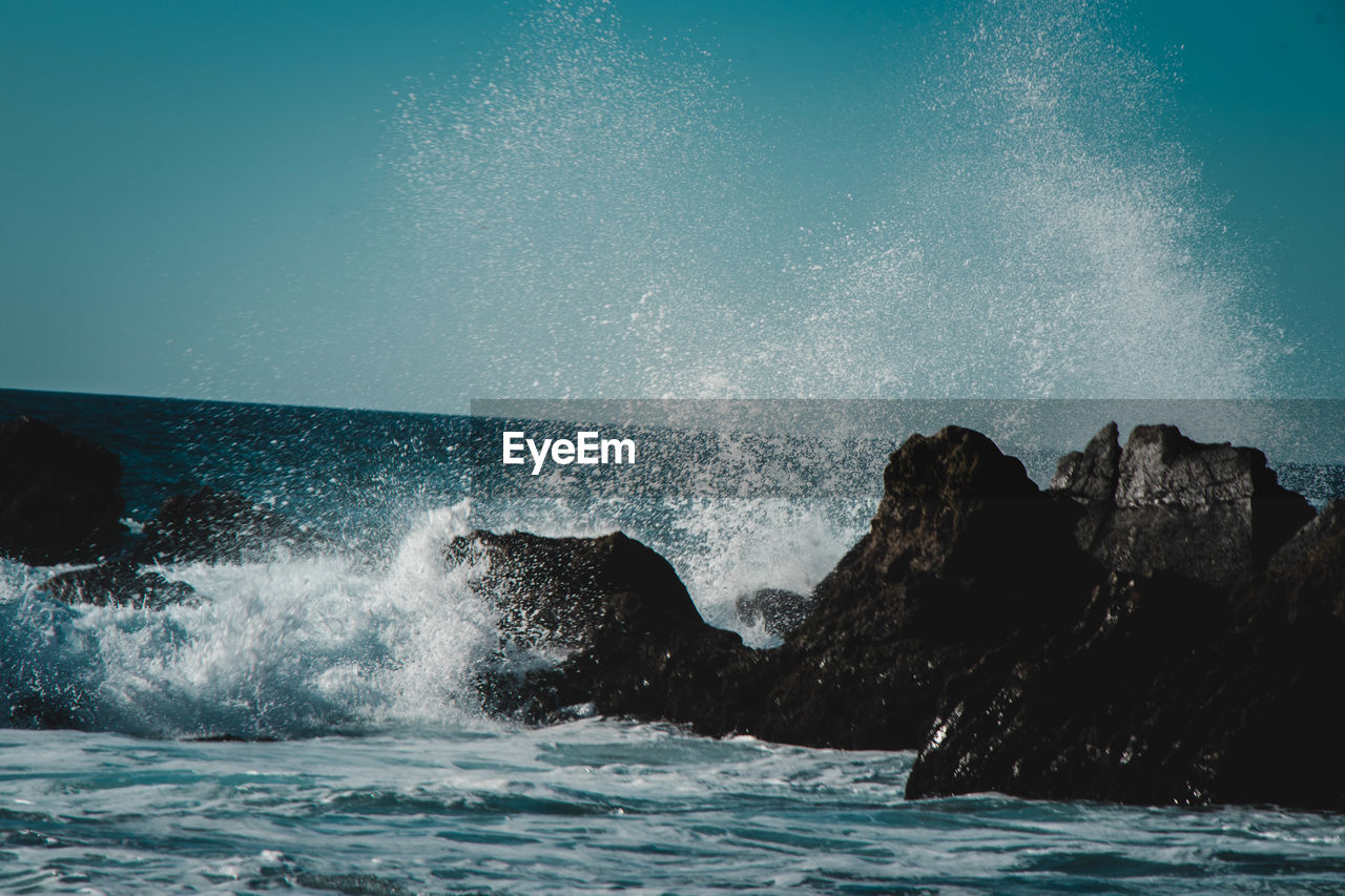 Waves splashing on rocks against sky