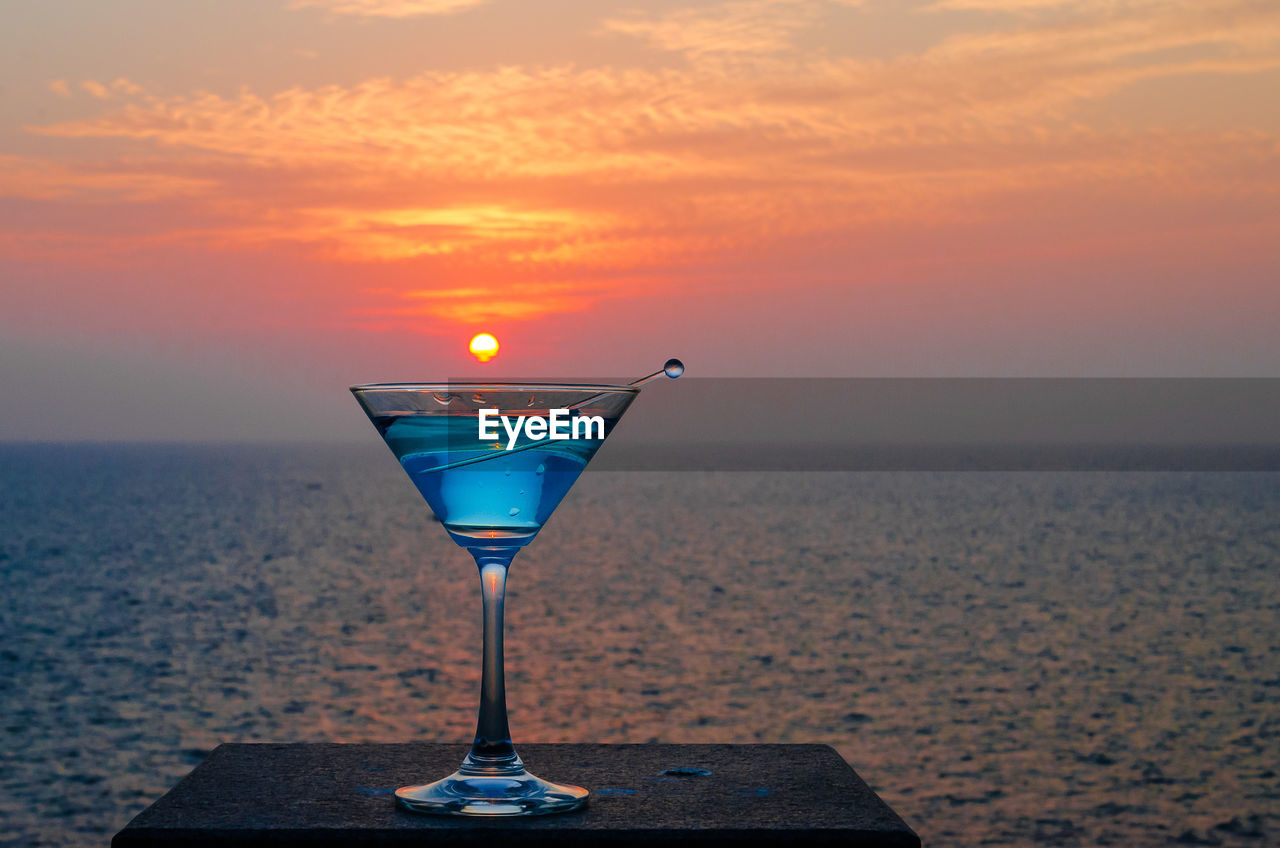 Close-up of martini glass against sea during sunset