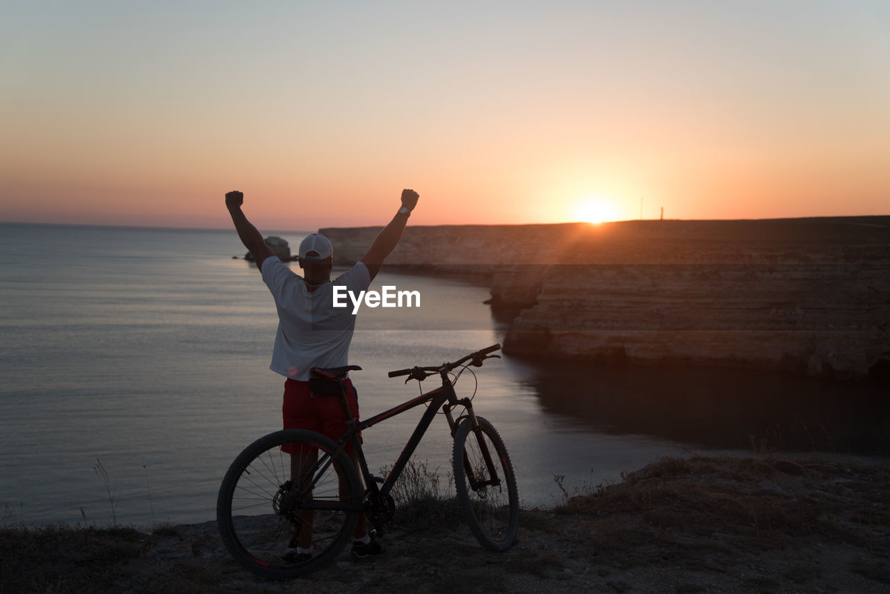 Rear view of man with bicycle by sea against sky