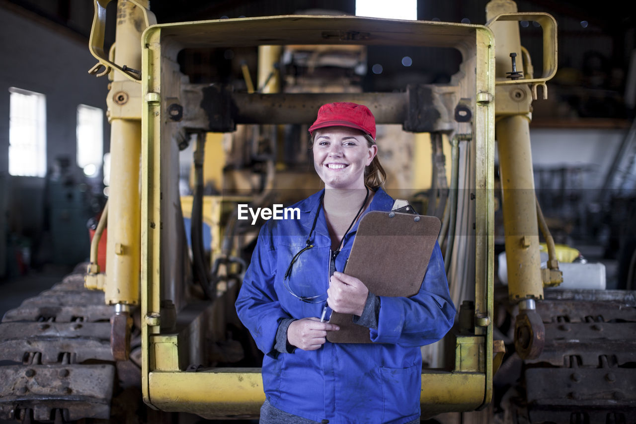 Portrait of smiling woman holding clipboard in workshop