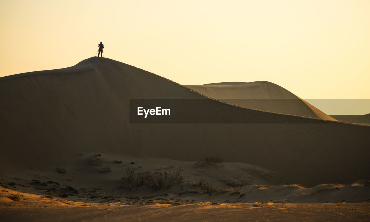 SILHOUETTE PERSON ON ARID LANDSCAPE AGAINST CLEAR SKY