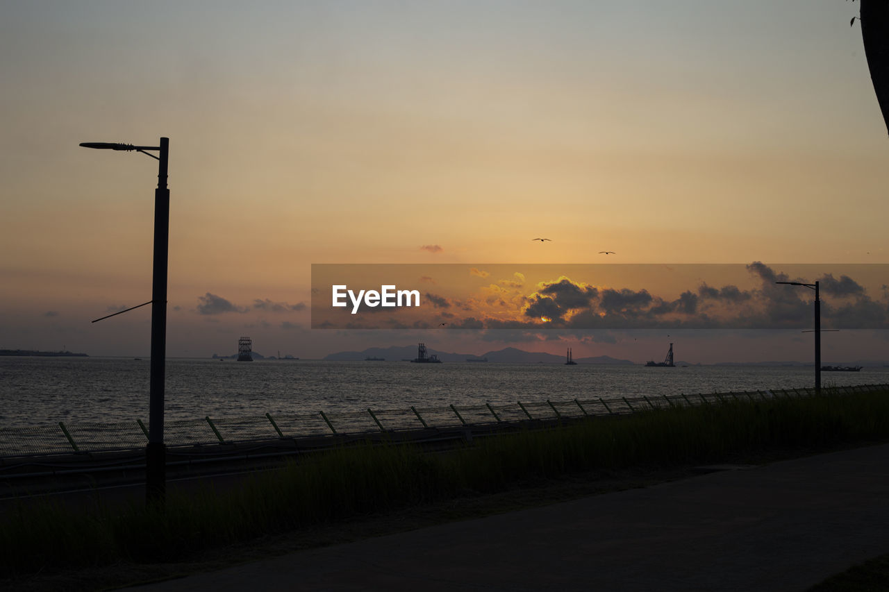 Silhouette street by sea against sky during sunset