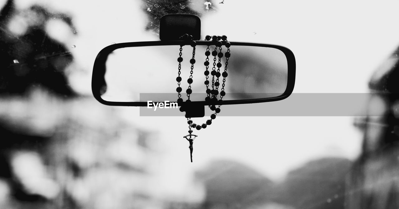 Close-up of rosary hanging on rear-view mirror in car