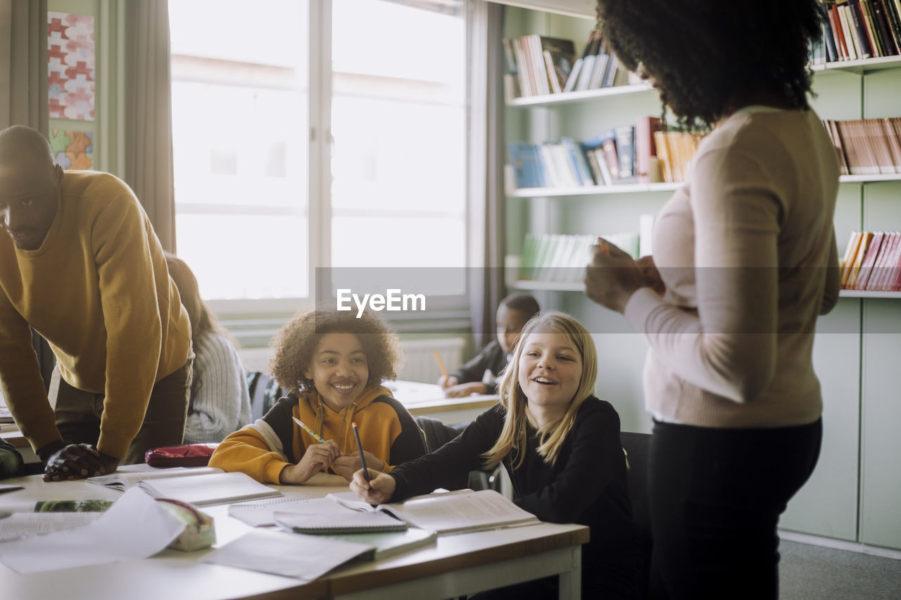 Smiling pupils interacting with teacher in classroom at school