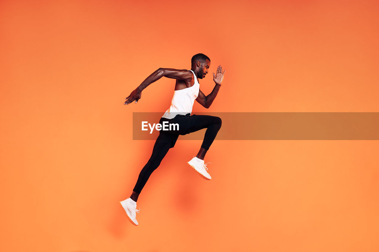 Full length of man jumping against orange background