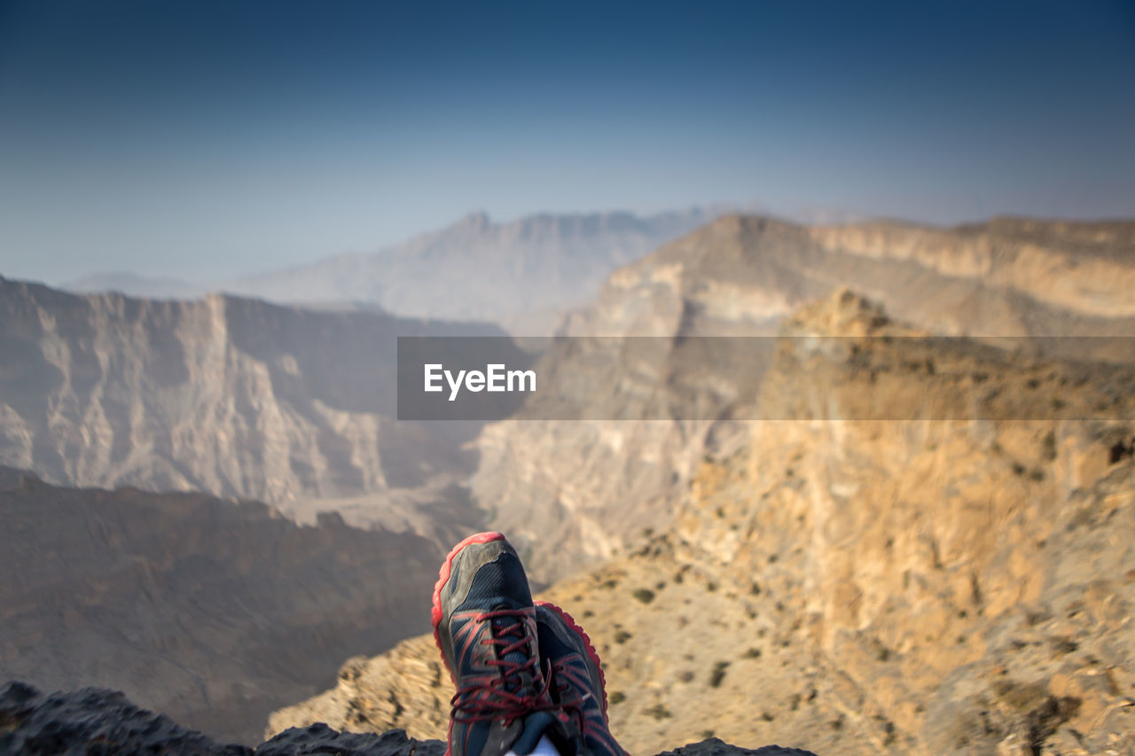 Low section of man wearing shoes on mountain against sky