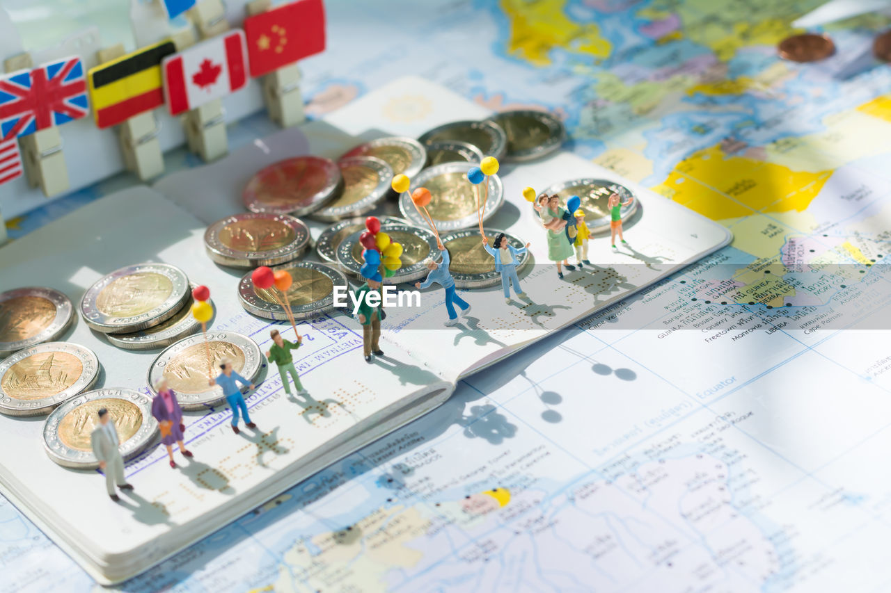 High angle view of figurines with coins and book on world map