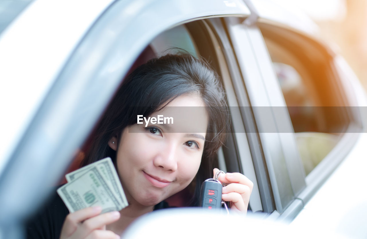 Portrait of woman holding key and paper currency in car