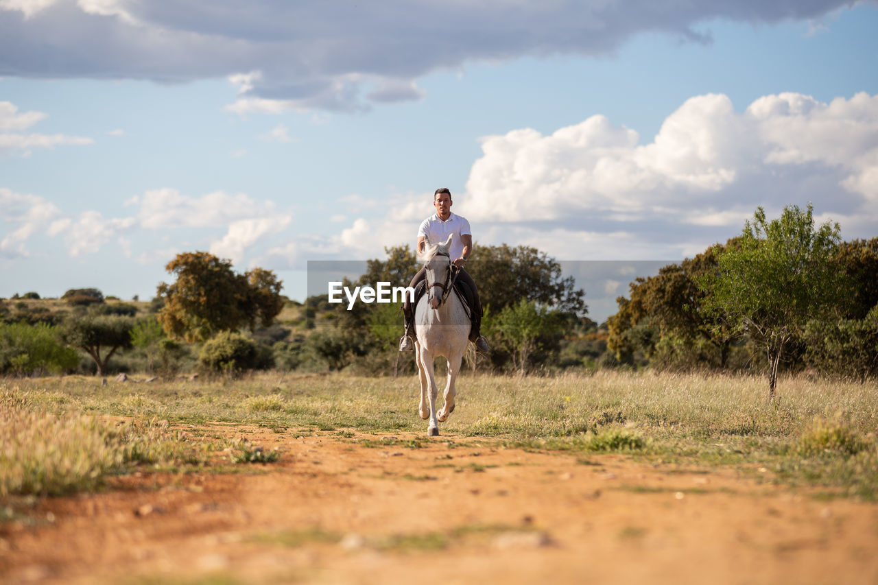 MAN RIDING HORSE STANDING ON FIELD