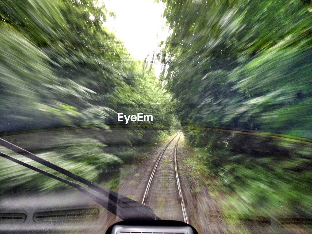 Railroad track amidst trees seen through wet windshield of locomotive