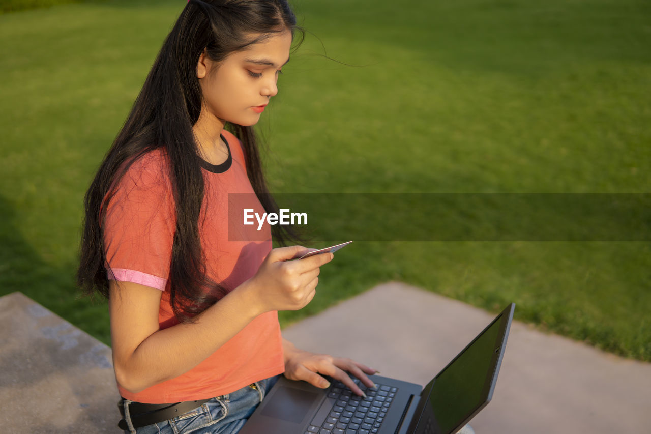 young woman using laptop while sitting on grassy field