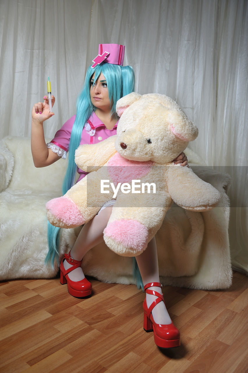 Young nurses with long blue hair injecting syringe to teddy bear at home