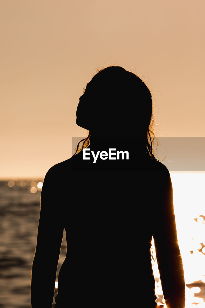 SILHOUETTE WOMAN STANDING ON BEACH AGAINST SKY DURING SUNSET