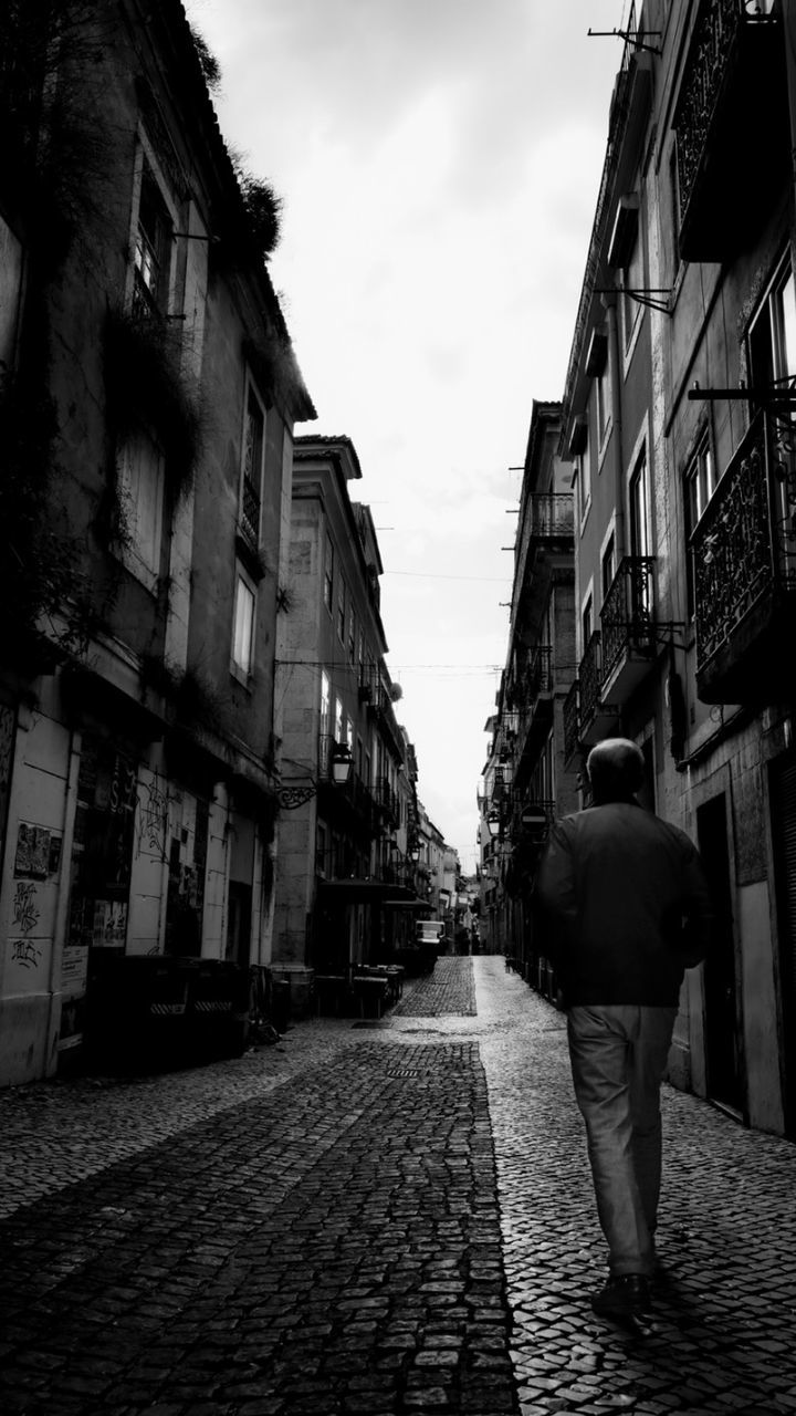 architecture, road, street, building exterior, black, built structure, city, alley, infrastructure, darkness, sky, rear view, monochrome, black and white, snapshot, full length, one person, white, building, walking, cobblestone, monochrome photography, urban area, adult, cloud, footpath, lifestyles, nature, the way forward, residential district, day, city life, outdoors, men, women, clothing
