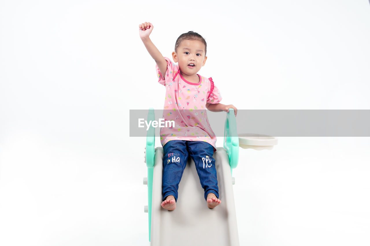 childhood, child, one person, happiness, smiling, full length, toddler, emotion, baby, white background, fun, portrait, front view, indoors, cheerful, cute, casual clothing, women, looking at camera, copy space, clothing, female, studio shot, lifestyles, arm, positive emotion, limb, joy, person, enjoyment, innocence, human limb, excitement, carefree, arms raised, cut out, holding, vitality, teeth, toy, smile