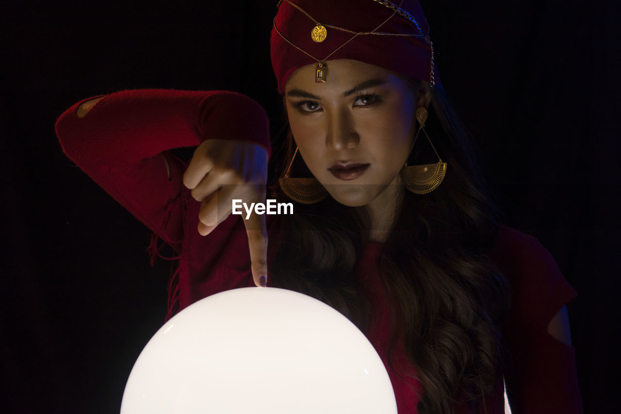 Portrait of female fortune teller pointing at sphere against black background