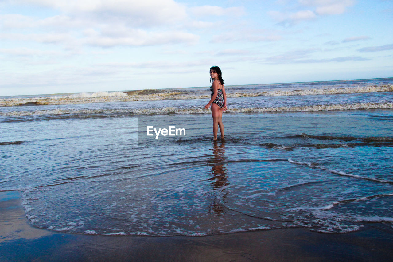 Rear view portrait of girl standing on beach against sky