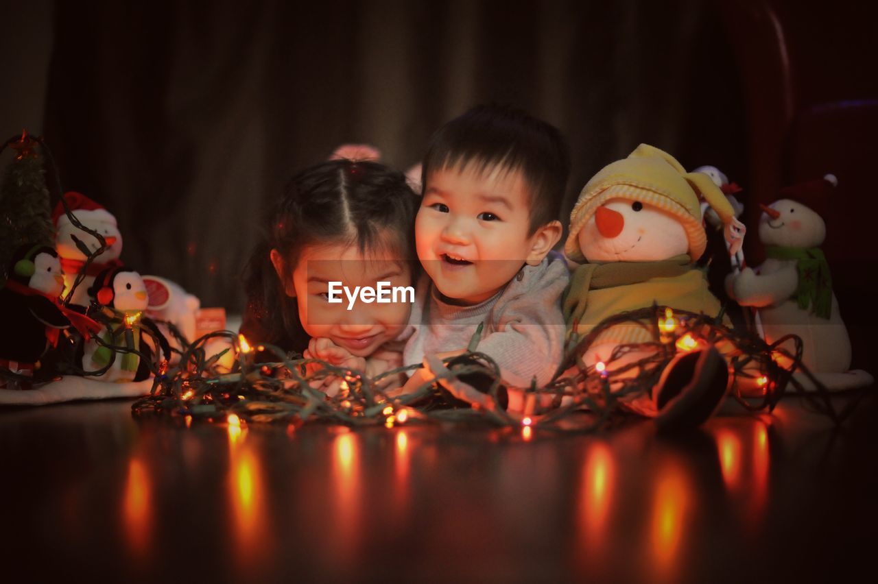 Portrait of cute siblings with illuminated string lights on floor