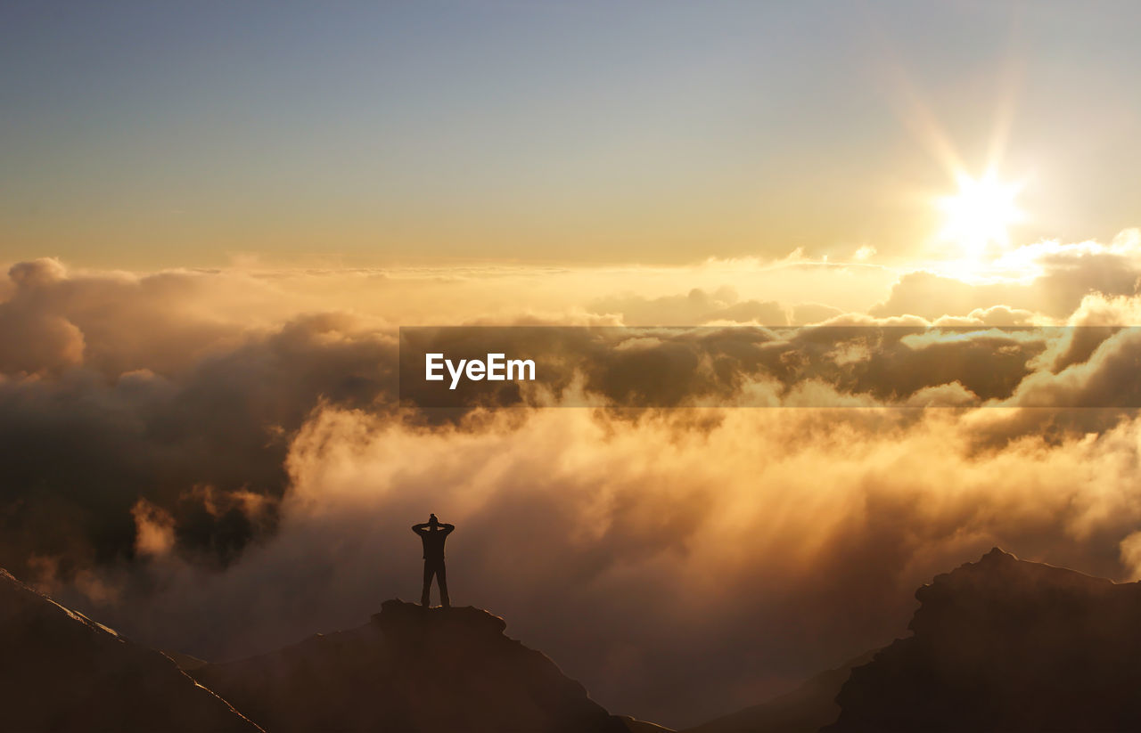 Silhouette of man standing on mountain peak in the clouds