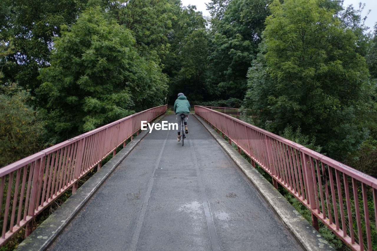 Rear view of woman riding bicycle on footbridge