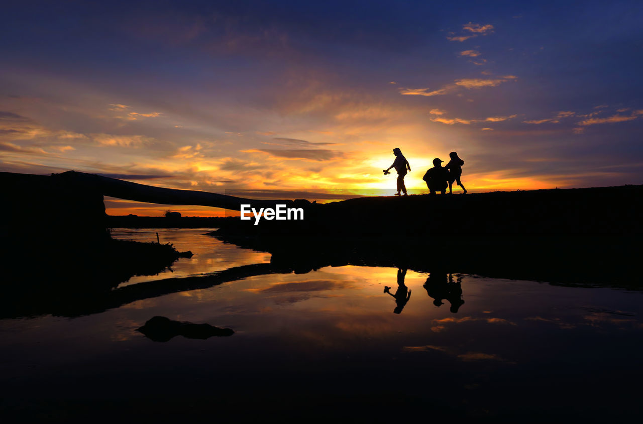 Silhouette people standing by lake against sky during sunset