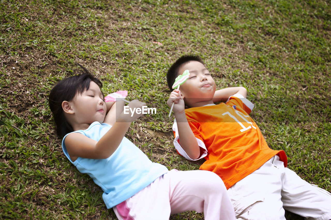 Friends eating candies while lying on field at park