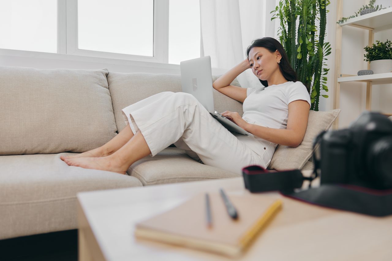 young woman using laptop while sitting on bed at home