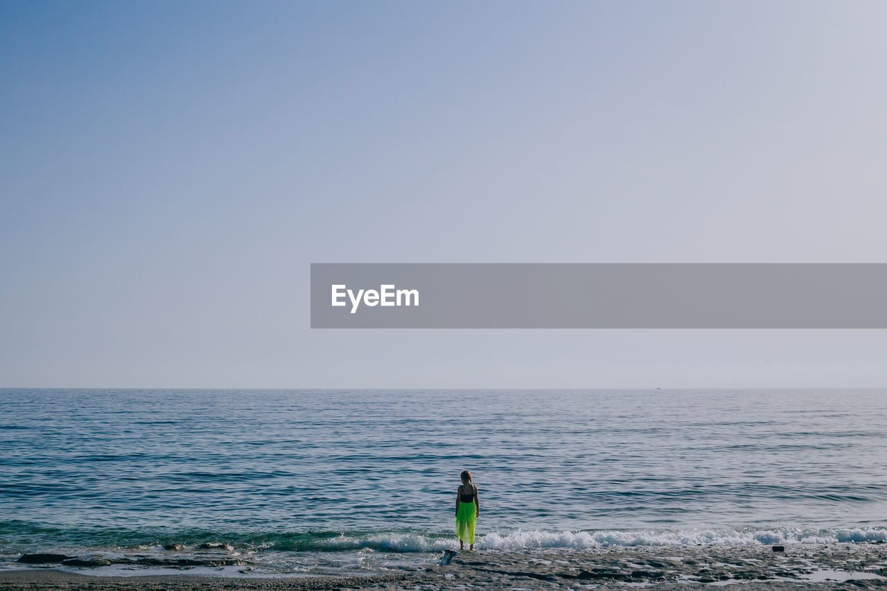 Rear view of girl standing at beach against clear sky