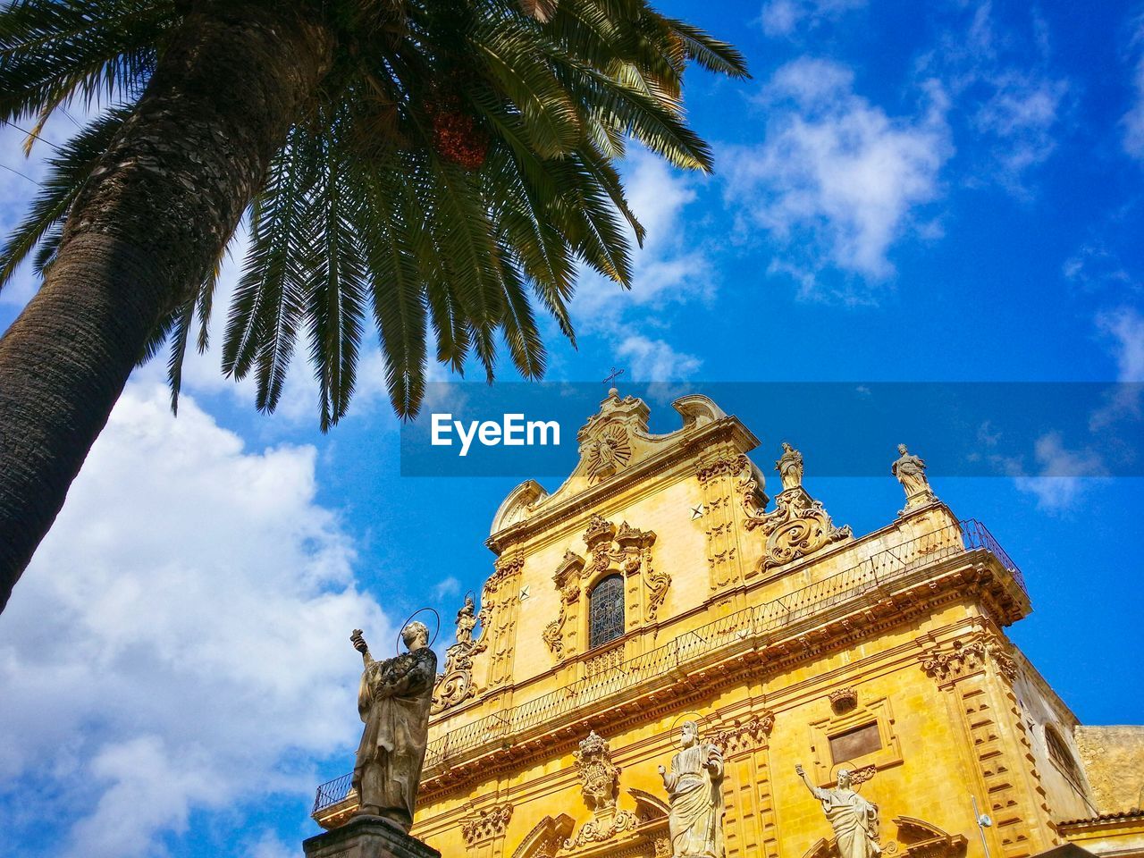 Low angle view of historic church by palm tree against sky