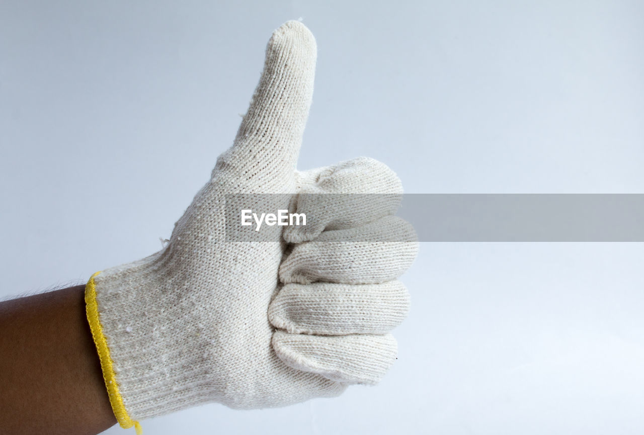 Close-up of hand wearing glove gesturing thumbs up against white background