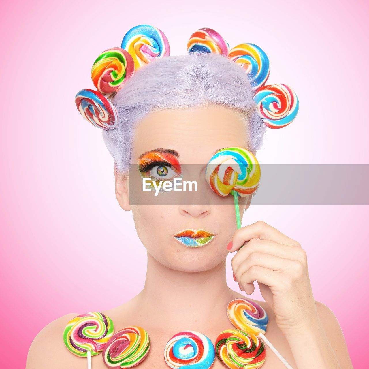 Portrait of young woman with multi colored candies against pink background