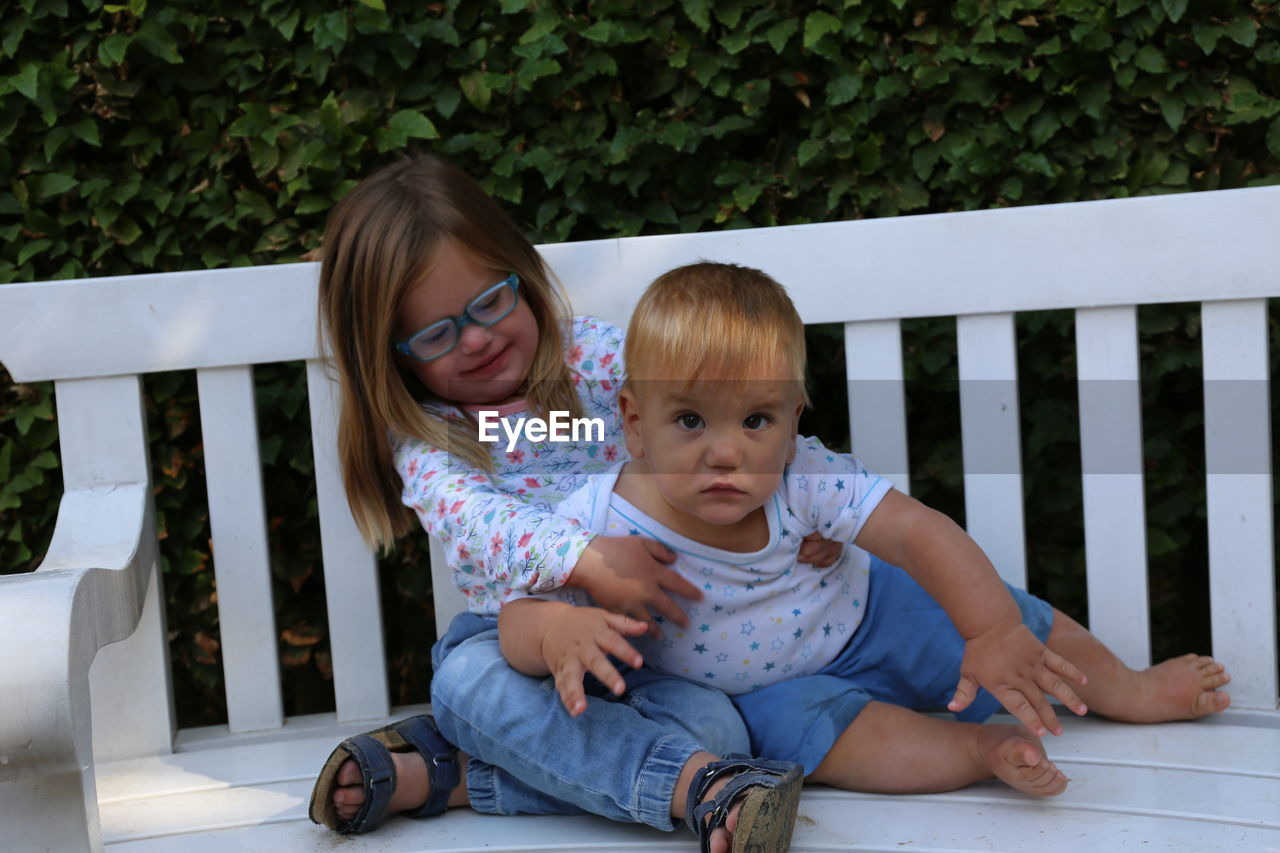 Siblings sitting on bench against plants