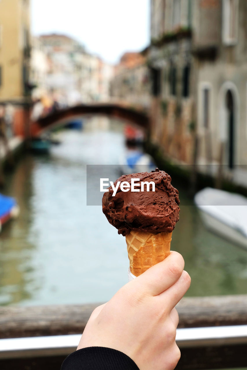 Close-up of hand holding ice cream cone against canal