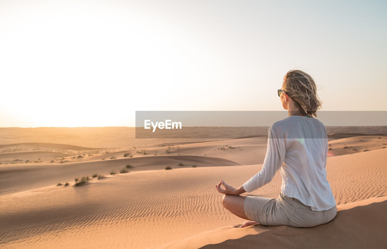 WOMAN SITTING ON SAND IN DESERT